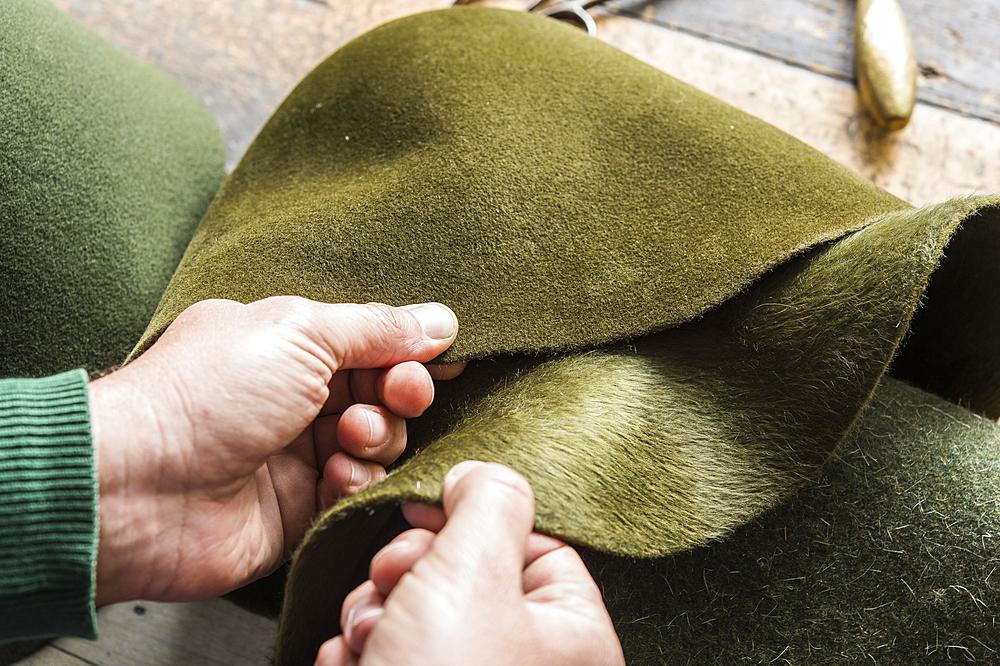 Hands checking different wool felt hat bodies, shades of green, on workbench, hatmaker workshop, Bad Aussee, Styria, Austria, Europe