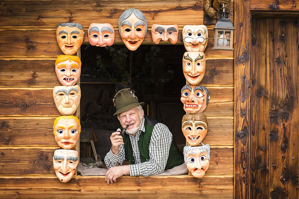 Wooden mask carver in a window, framed by painted wooden masks, wooden mask carving workshop, Bad Aussee, Styria, Austria, Europe