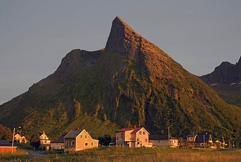 The houses of Ersfjord illuminated by the last light of the day below the peak of a mountain on the island of Senja, Troms, Norway, Europe