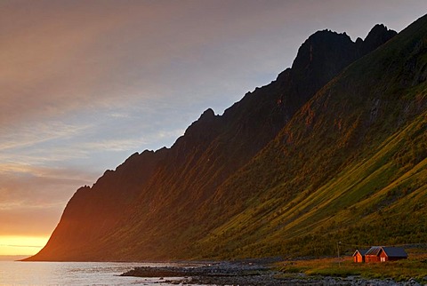 Sun set over the Norwegian Sea behind typical red Rorbuer huts, rorbu, near Ersfjord on the island of Senja, Troms, Norway, Europe