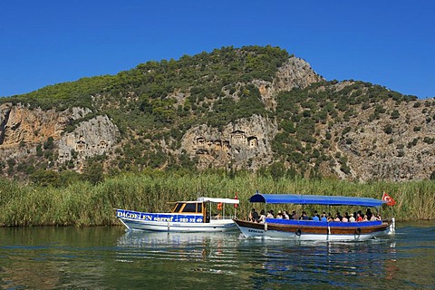 Excursion boats on the Dalyan river in front of the rock tombs of Caunos or Kaunos near Marmaris, Turkish Aegean Coast, Turkey