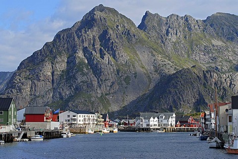 The steep rocks of the Lofoten archipelago behind the fishing boats and typical red and white houses in HenningsvÃŠr, Nordland, Norway, Europe