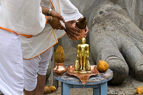 Two Jain pilgrims are pouring water over a small statue at the feet of the statue of Lord Gomateshwara, the tallest monolithic statue in the world, dedicated to Lord Bahubali, carved out of a single block of granite stone, 18 meters high, 983 AD, Sravanab