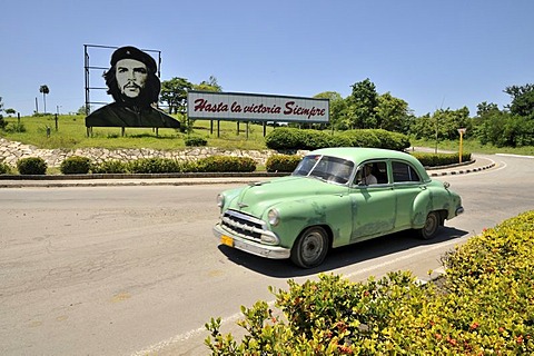 Vintage car in front of revolutionary propaganda, "Hasta la victoria siempre", Spanish for "ever onward to victory" with portrait of Ernesto "Che" Guevara, Las Tunas, Cuba, Caribbean