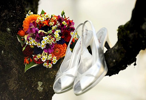 Bridal bouquet and silver wedding shoes hanging from a tree