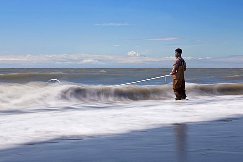 Surf zone with a fisherman on the beach in Kenai on the Kenai Peninsula with Mount Redoubt volcano in the Cook Inlet, Alaska, USA