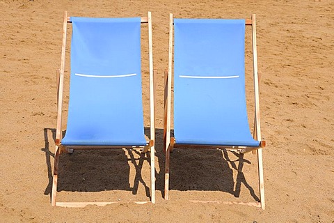 Two blue wooden deckchairs on the beach