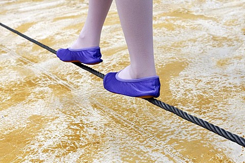 Little girl in ballet shoes balancing on a steel cable just above the ground