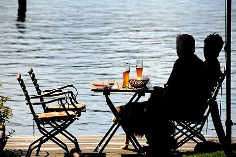 Snack beside the lake, silhouettes of two people sitting at a table, Lake Ratzeburg, Ratzeburg, Schleswig-Holstein, Germany, Europe