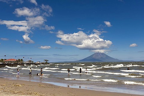 People walking on the shallow shore of Lago de Nicaragua with the volcanic island of Ometepe and the stratovolcano Volcan Concepcion at back, San Jorge, Nicaragua, Central America