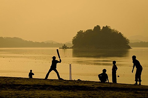 Teenagers playing cricket, the national game of India, on the bank of the Brahmaputra river, Peacock Island and the Uma Nanda Temple at the back, Guwahati, Assam, India, Asia