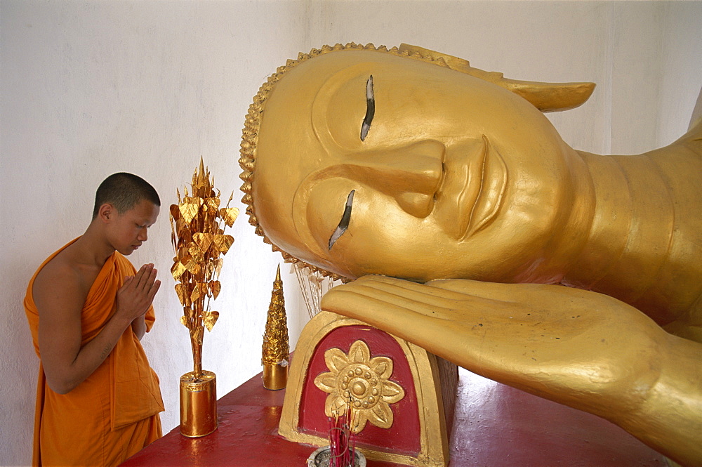 Novice monk praying at Reclining Buddha, Wat Pha Baat Tai, Luang Prabang, Laos, Indochina, Southeast Asia, Asia