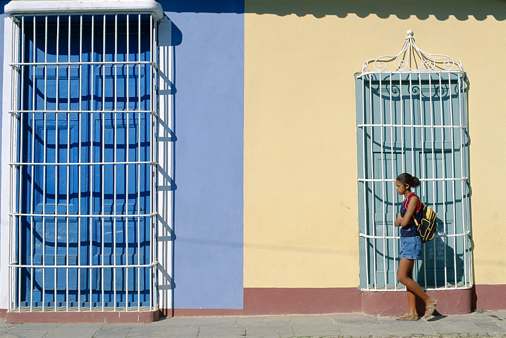 Young woman walking past colonial grille windows, Trinidad, UNESCO World Heritage Site, Cuba, West Indies, Central America