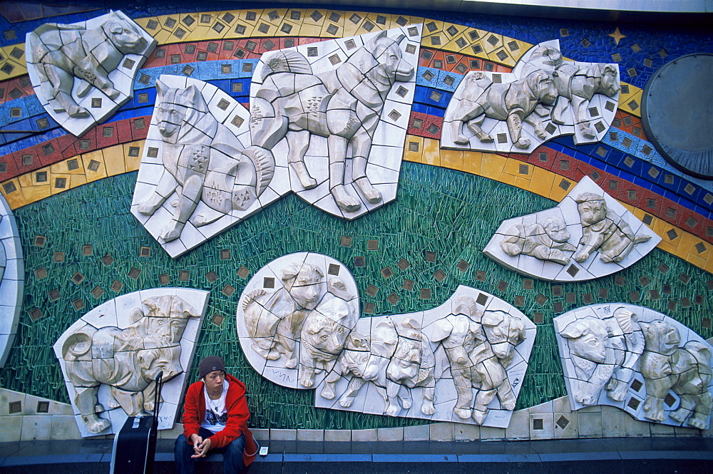 Young man sitting under Hachiko Dog mural, Shibuya, Tokyo, Japan, Asia