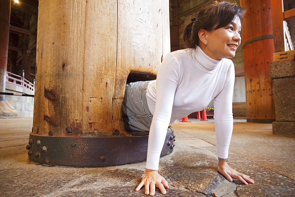 Tourist squeezing through the healing pillar for good health, Todaiji Temple, Nara, Japan, Asia