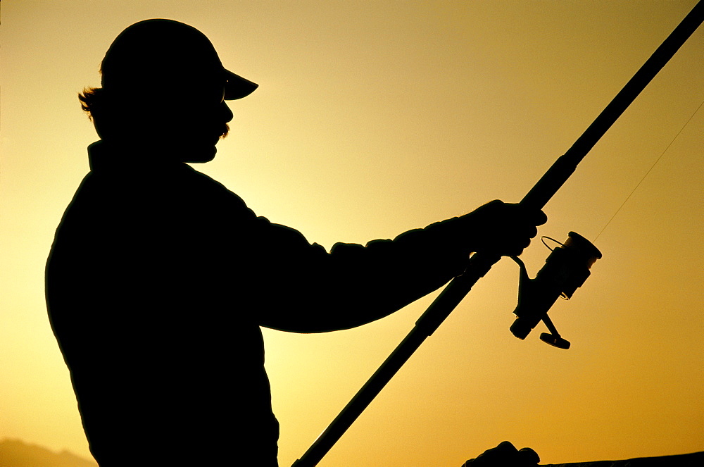 Silhouette of fisherman casting fishing line at sunset