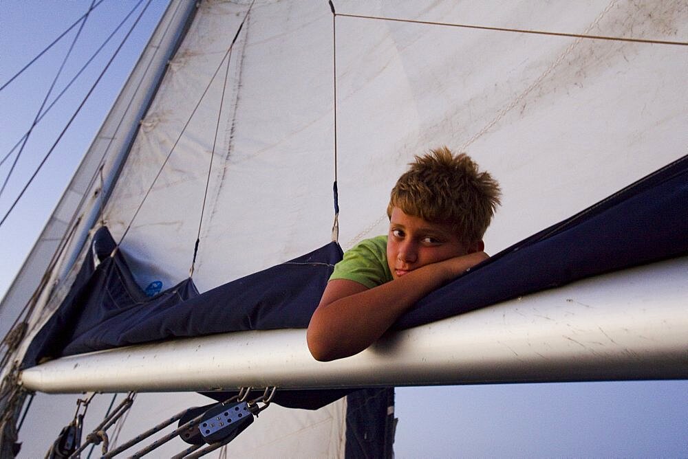 Young boy lying on the main sail of a sailing boat on the Mediterranean sea