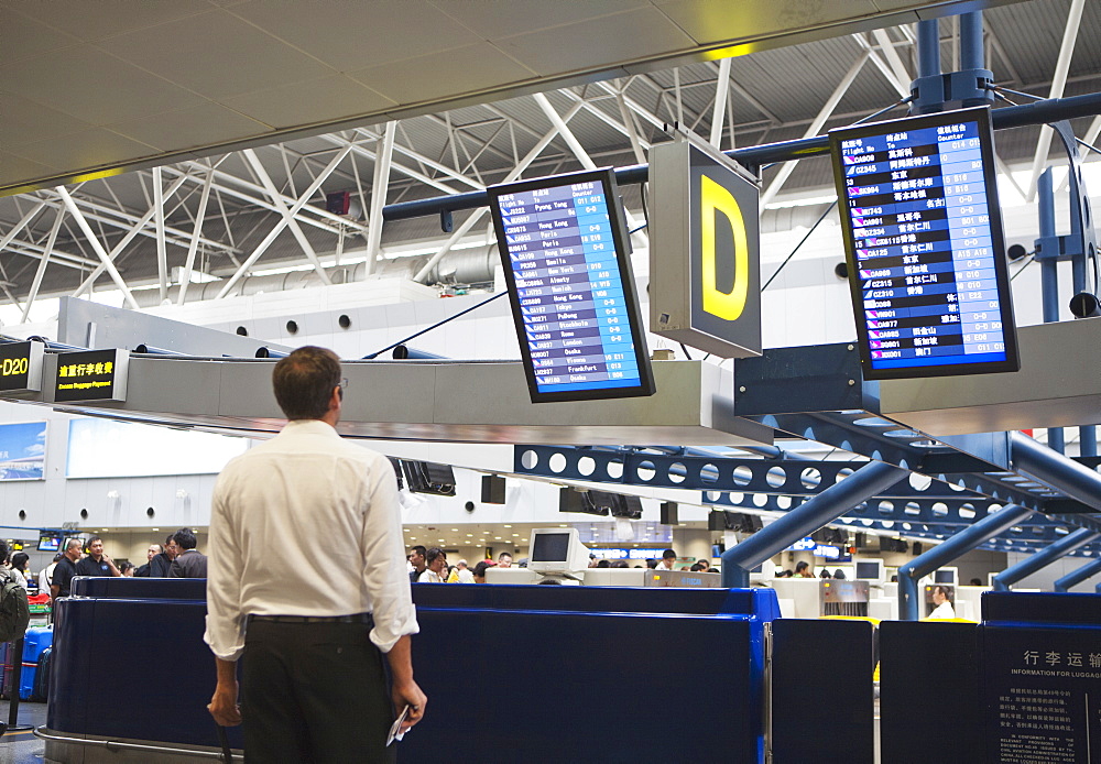 A airline traveler in an airport reading the plane departure signage, Beijing, China, Asia