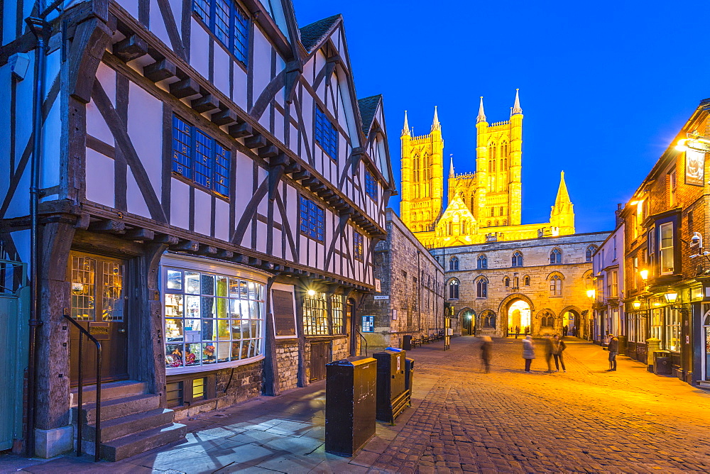 View of illuminated Lincoln Cathedral viewed from Exchequer Gate with timbered architecture of Visitors Centre at dusk, Lincoln, Lincolnshire, England, United Kingdom, Europe