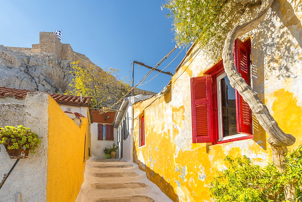 View of pastel coloured houses in Plaka District of Athens, overlooked by the walls of The Acropolis, Athens, Greece, Europe