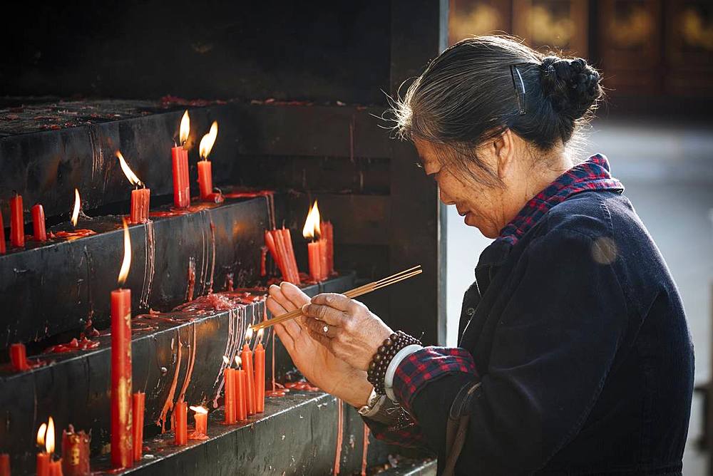 Woman lighting candles at Yuantong Buddhist Temple, Kunming, Yunnan Province, China, Asia