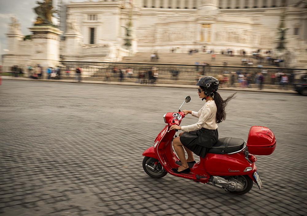 Young woman riding Vespa moped through streets in front of Vittorio Emanuele Monument, Rome, Lazio, Italy, Europe