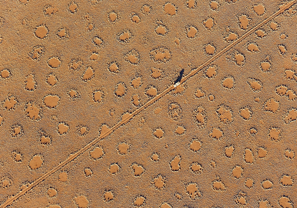 A vehicle of the balloon ground crew tries to follow the flight direction of the hot-air balloon, crossing a sandy plain at the edge of the Namib Desert. The so-called 'Fairy Circles' are circular patches without any vegetation which according to recent s