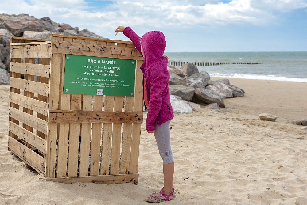 Girl throwing a plastic waste in a tidal bin on a beach on the Opal Coast, summer, Pas de Calais, France