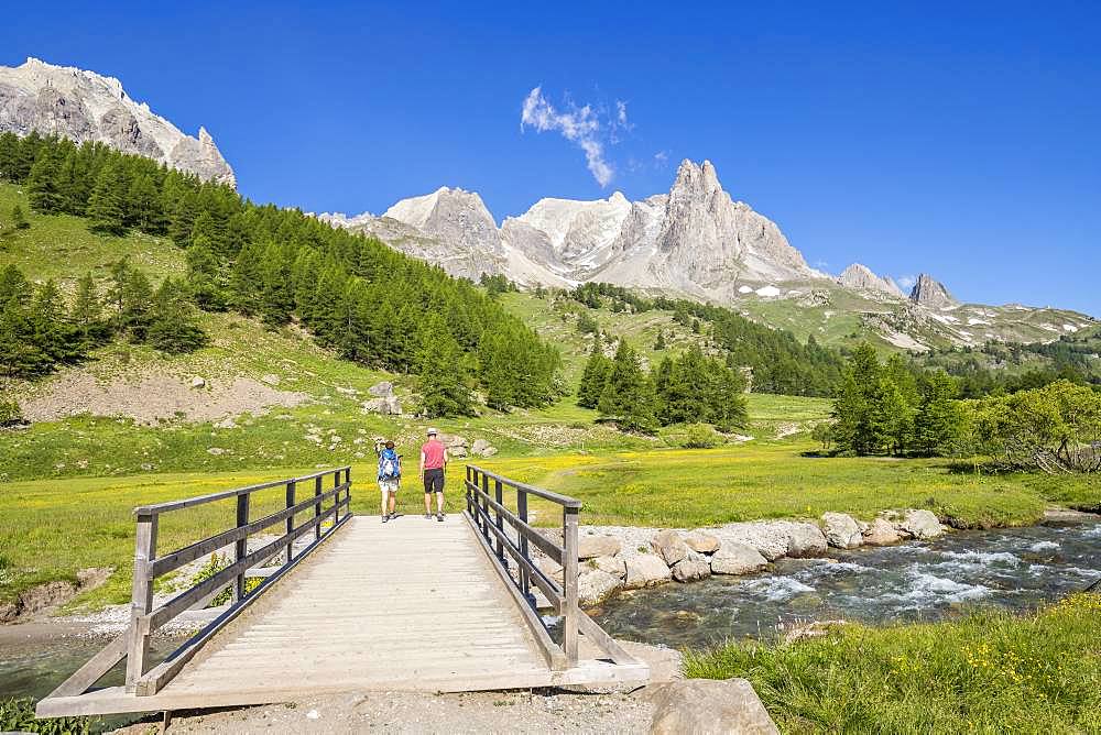 Vallee de La Claree, hikers on the Pont du Moutet, in the background the massif of Cerces (3093m) and the peaks of the Main of Crepin (2942m), Nevache, Hautes-Alpes, France