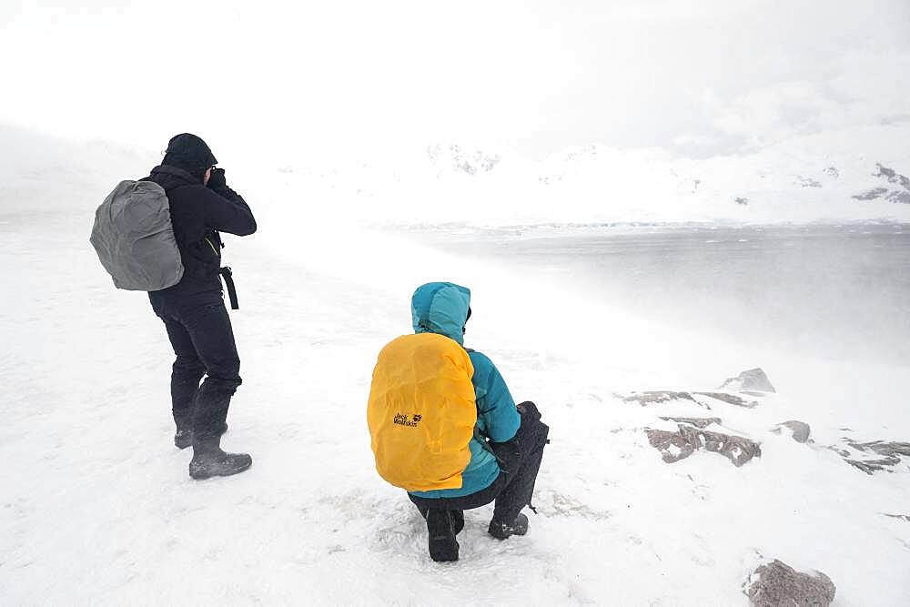 A snowstorm hits two tourists watching the landscape in Neko Harbour, Antarctica.