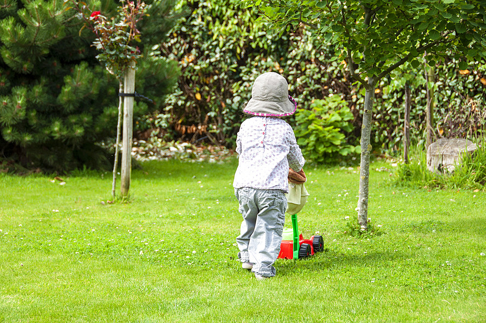 Girl playing with her lawnmower in a garden, summer, Pas-de-Calais, France