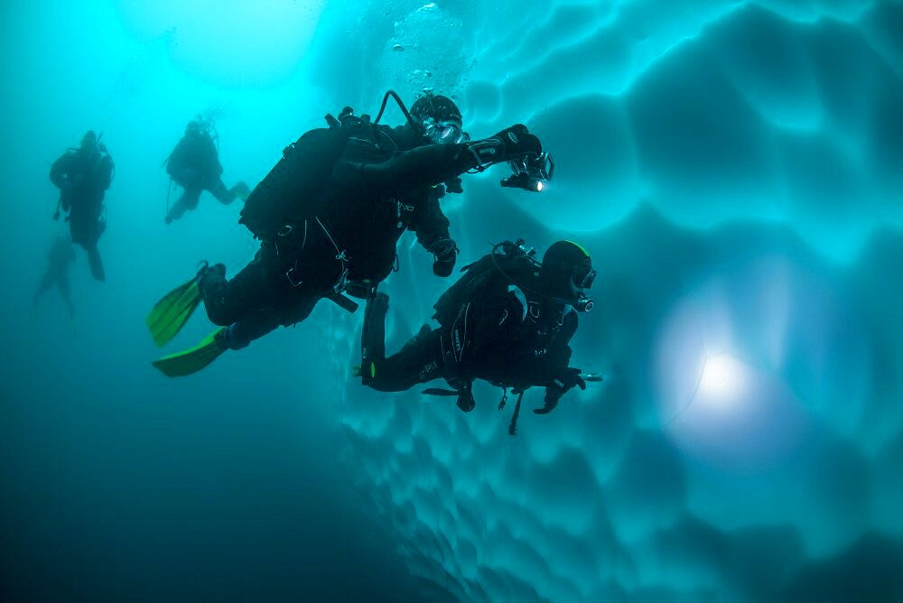 Scuba divers diving around the underwater part of a iceberg, Antarctic Peninsula, Antarctica