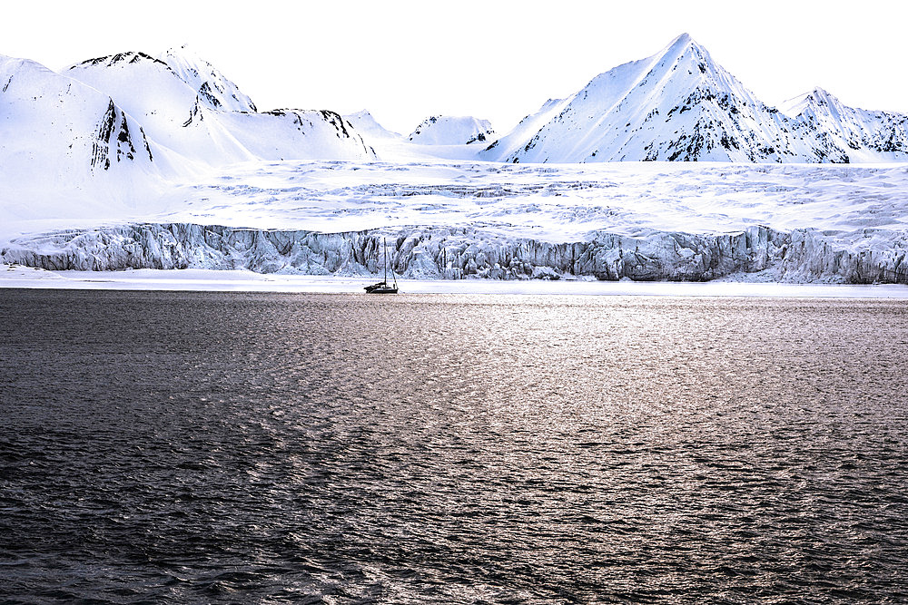 Landscape of Svalbard in Norway, also known as Spitsbergen. This territory stretches from latitude 75 to 80 degrees to the pack ice a few hundred kilometers from the North Pole. Melting ice, early global warming. Front of a glacier fracturing at the edge of a fjord. Explorers' sailboat at the ice edge