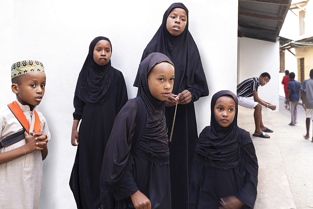 Traditional Muslim children: girls wear abayas, boys wear kofias, traditional hats, on their way to school in the narrow streets of Stone Town, capital of Zanzibar, Tanzania.