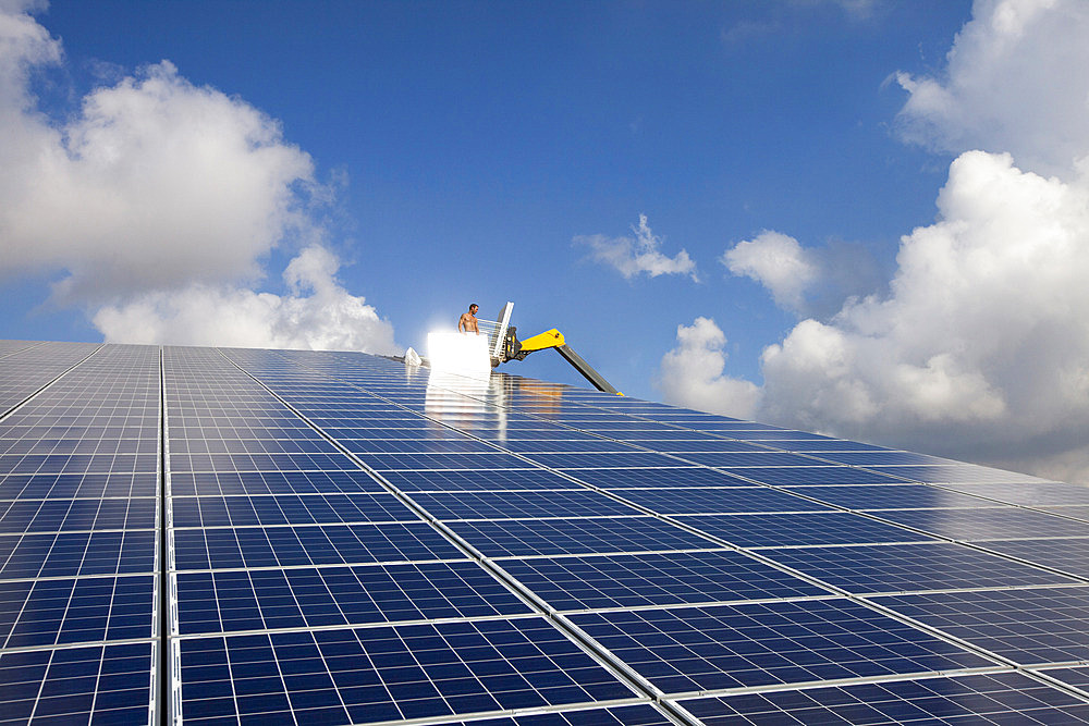 Photovoltaic panels installed on the roof of a farm building against a blue sky with light clouds, France