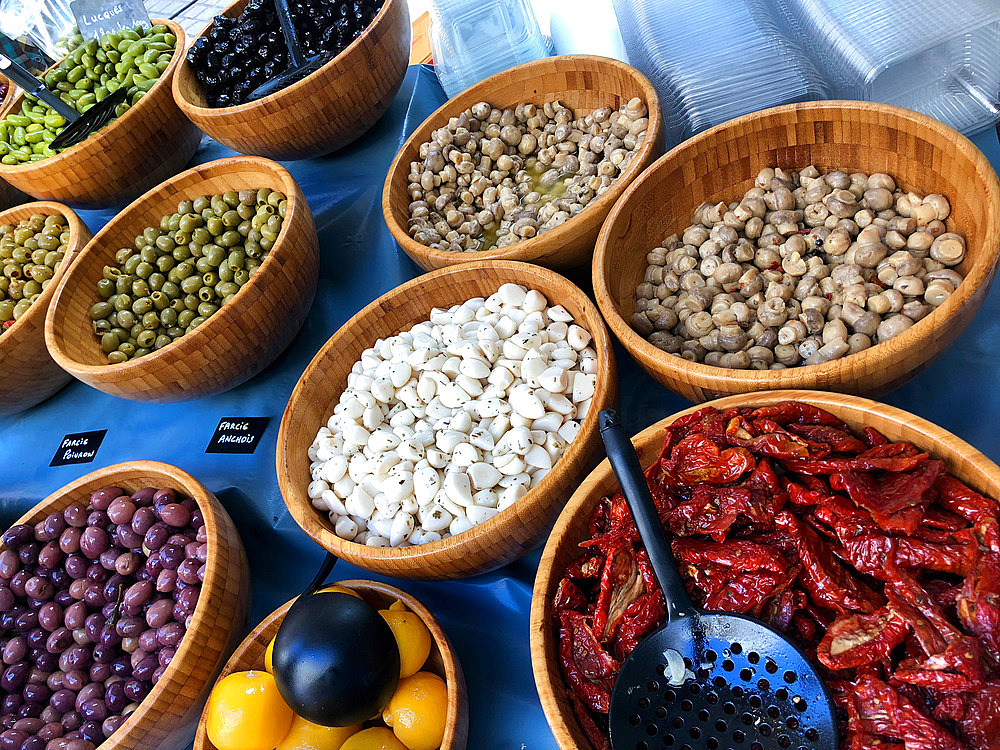 Olives, sun-dried tomatoes, vinegared mushrooms, preserved lemons on a Market stall, in their olive wood container,