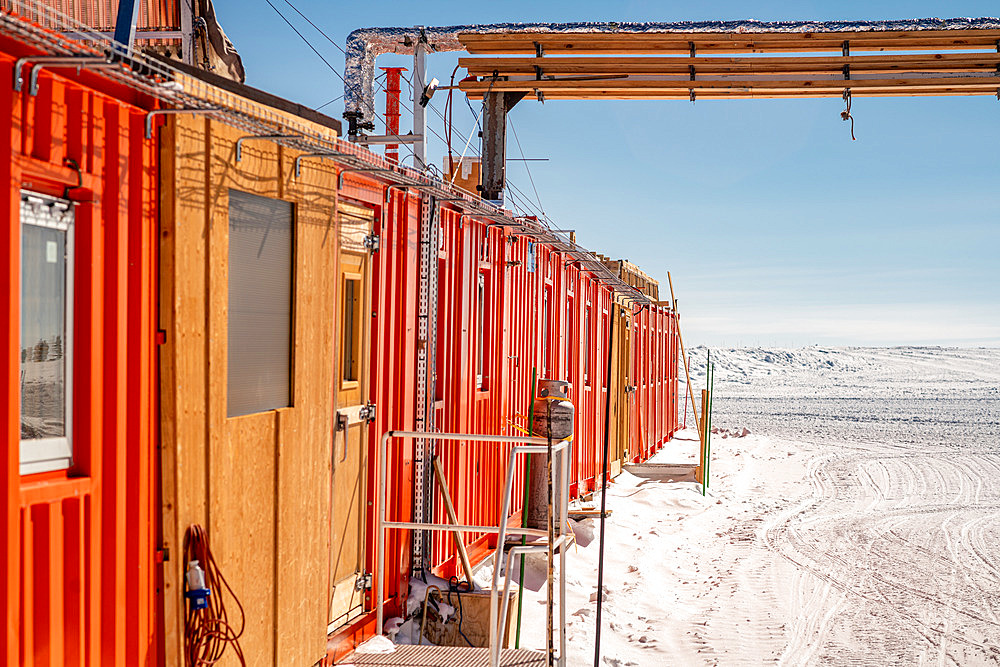 Building made of containers lined up in a row, powered by pipes and electric cables. The summer camp is made up of containers assembled together. It was built in the early 1990s. Since then, irregular ground settlement has caused the building to deform. It is now used as a summer dormitory. Concordia Antarctic Research Station, Dome C plateau, East Antarctica.