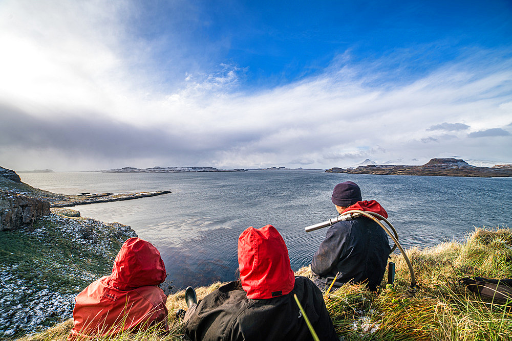 A contemplative break for the team of scientists. The ornithologist on the right has a camera to inspect the inside of the burrows to read the rings of banded birds. Mayes Island, Gulf of Morbihan. Kerguelen Archipelago.
