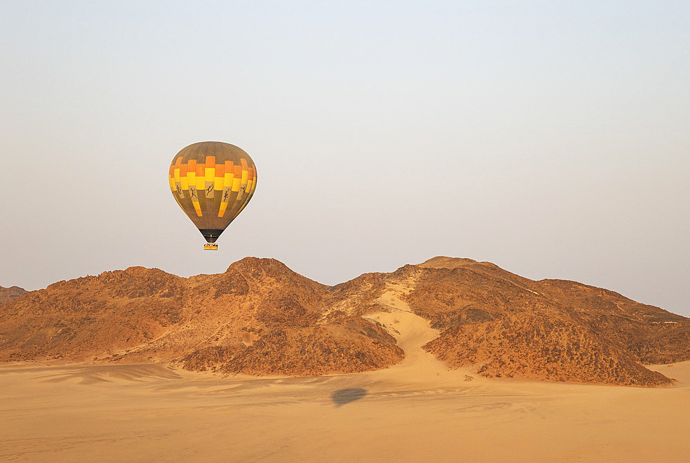 The hot-air balloon above an arid plain and isolated mountain ridges at the edge of the Namib Desert. Aerial view from a second balloon. Namibia.