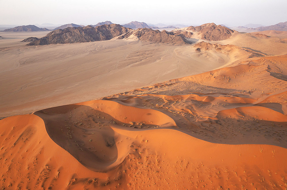 Sand dunes and mountain ridges in the Namib Desert. In the evening. Aerial view. Namib-Naukluft Park, Namibia.