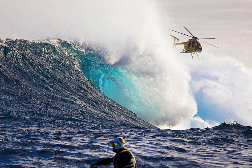 A helicopter filming a tow, in surfer at Peahi Jaws off Maui Hawaii The head in the foreground is driving a jetski