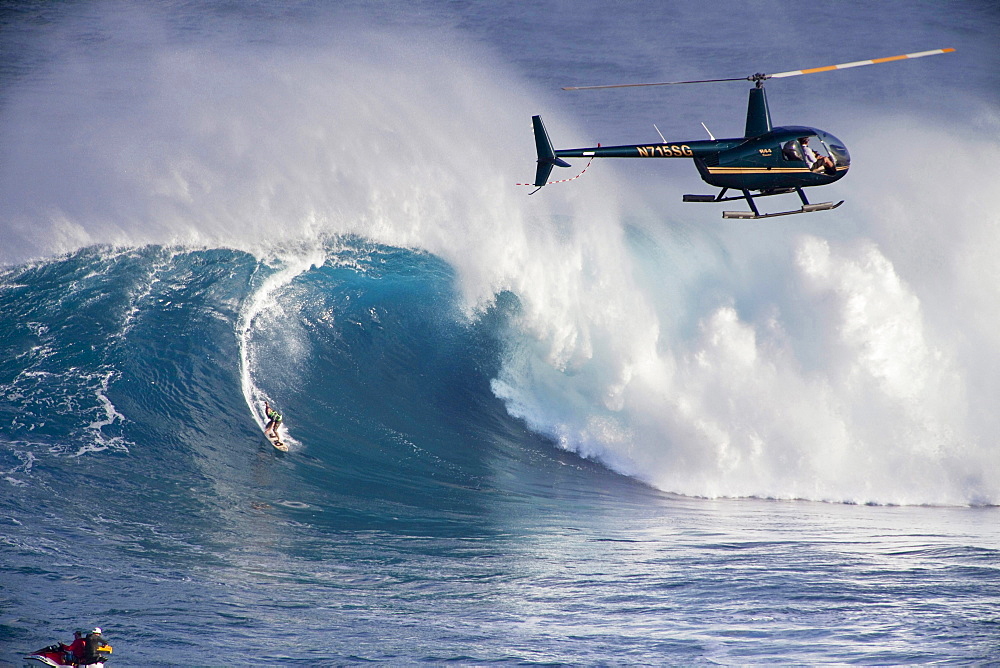 A helicopter filming a tow, in surfer at Peahi Jaws off Maui Hawaii