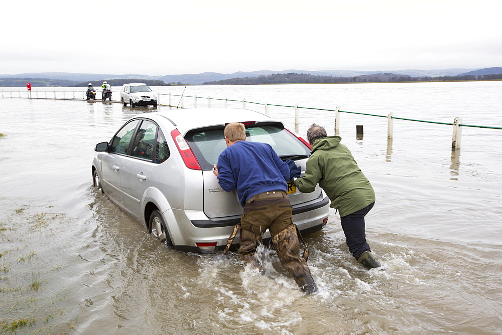 A motorist stuck in flood waters on the road at Storth on the Kent Estuary in Cumbria, UK, during the January 2014 storm surge and high tides, is pushed out by two helpers.