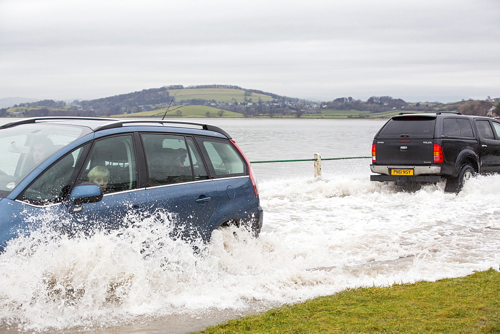 A motorist travels through flood waters on the road at Storth on the Kent Estuary in Cumbria, UK, during the January 2014 storm surge and high tides.