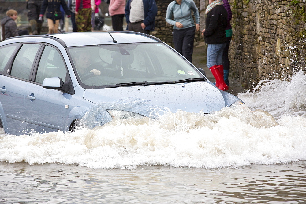 A motorist travels far too fast through flood waters on the road at Storth on the Kent Estuary in Cumbria, UK, during the January 2014 storm surge and high tides.