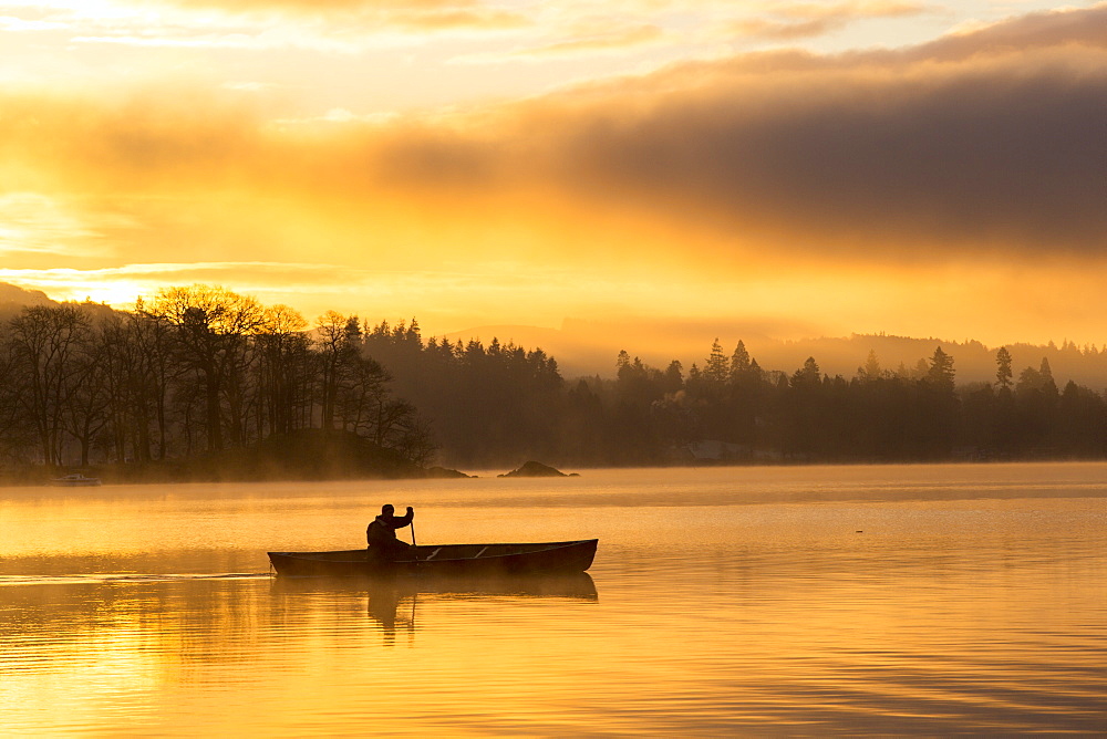 Sunrise over Lake Windermere in Ambleside, Lake District, UK, with a man paddling a Canadian Canoe.