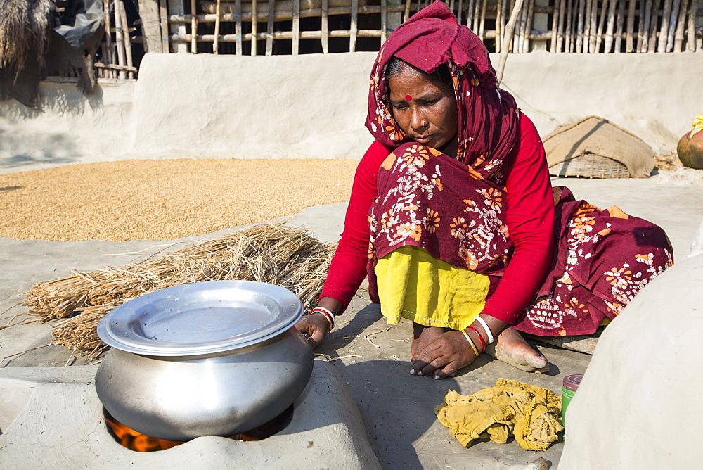 A woman subsistence farmer cooking on a traditional clay oven, using rice stalks as biofuel in the Sunderbans, Ganges, Delta, India. the area is very low lying and vulnerable to sea level rise. All parts of the rice crop are used, and the villagers life is very self sufficient, with a tiny carbon footprint.