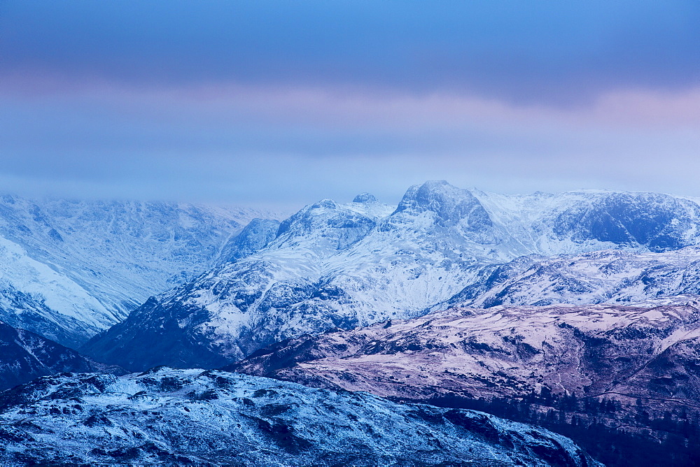 Reflected light from a hole in the cloud at sunset, creating a warm glow looking towards the Langdale Pikes from Wansfell in the Lake District, UK