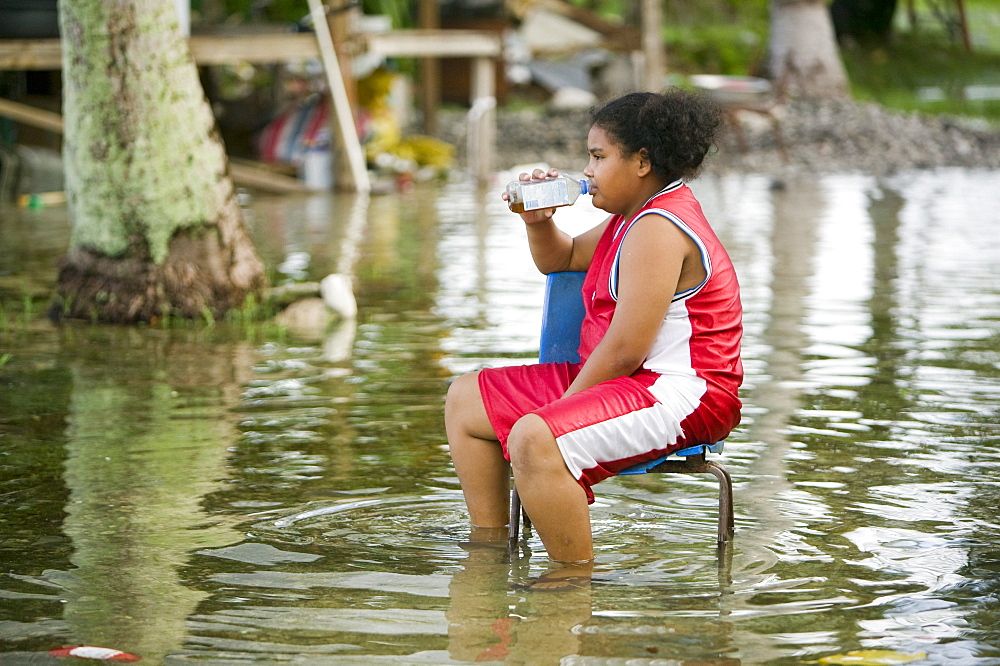 A teenage girl sits in the floodwater caused by sea water incursion due to global warming induced sea level rise that threatens the future of these low lying islands, Funafuti Atoll, Tuvalu, Pacific