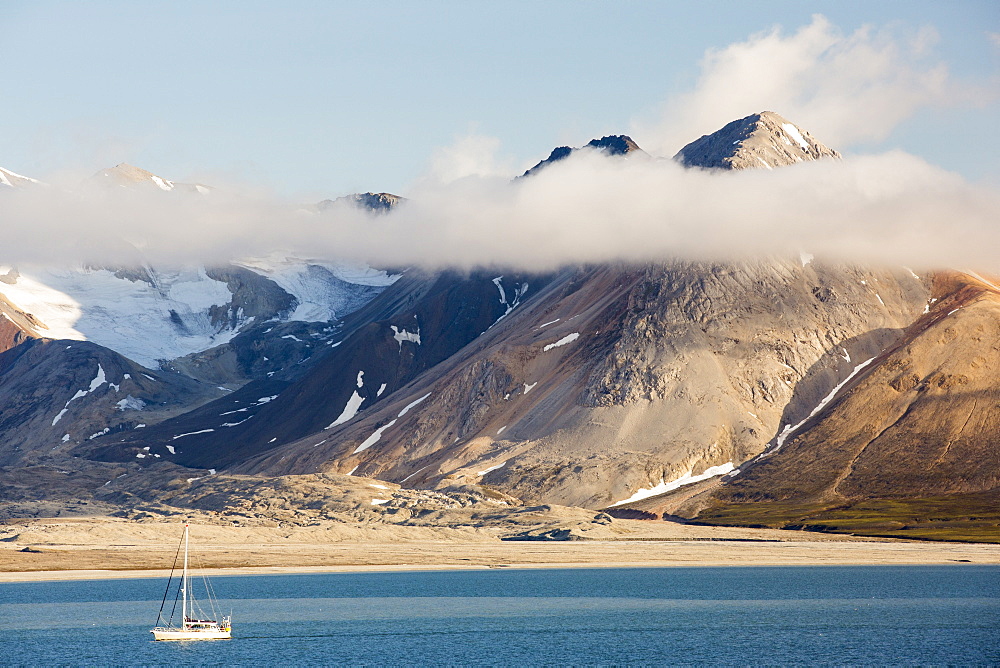 A mountain peak, peeping through the cloud at Bourbonhamna 77¬8 33‚Äôn 15¬8 00‚Äôe Spitsbergen; Svalbard, with a yacht sailing past.